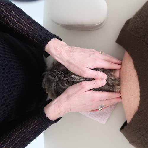 Handen die reiki geven in de nek van persoon die op een behandeltafel ligt